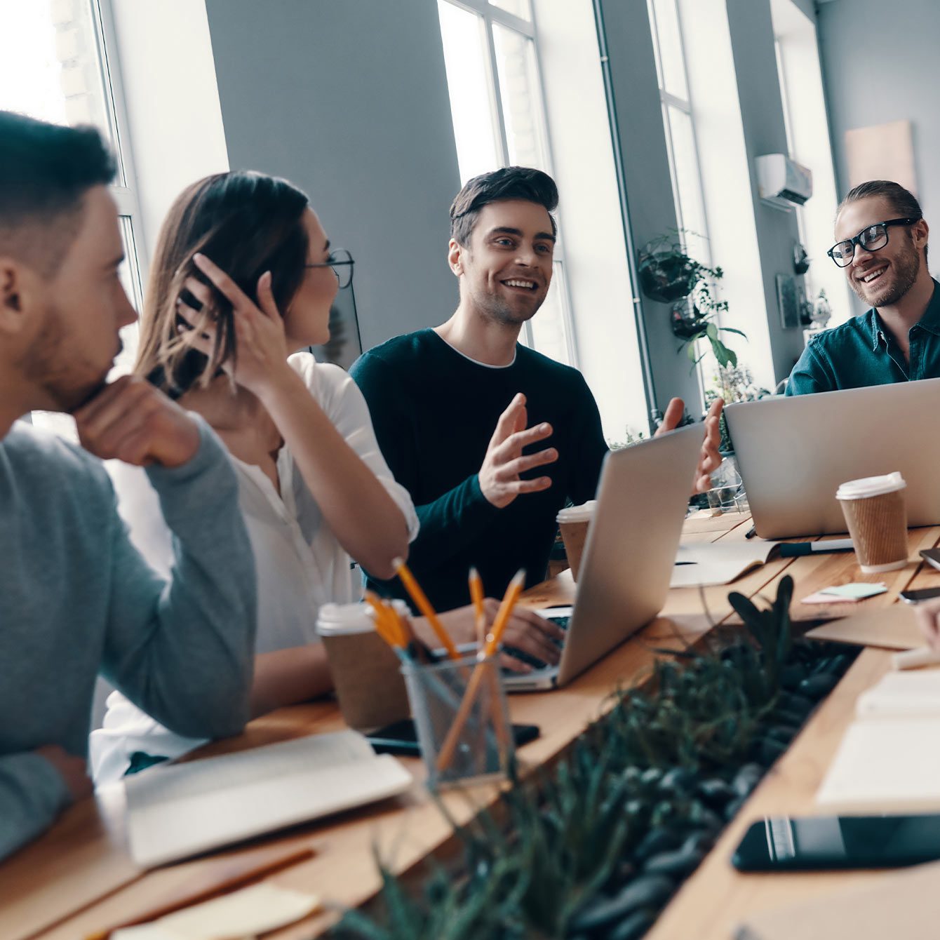 Group of young modern people discussing something and smiling while working in the creative office